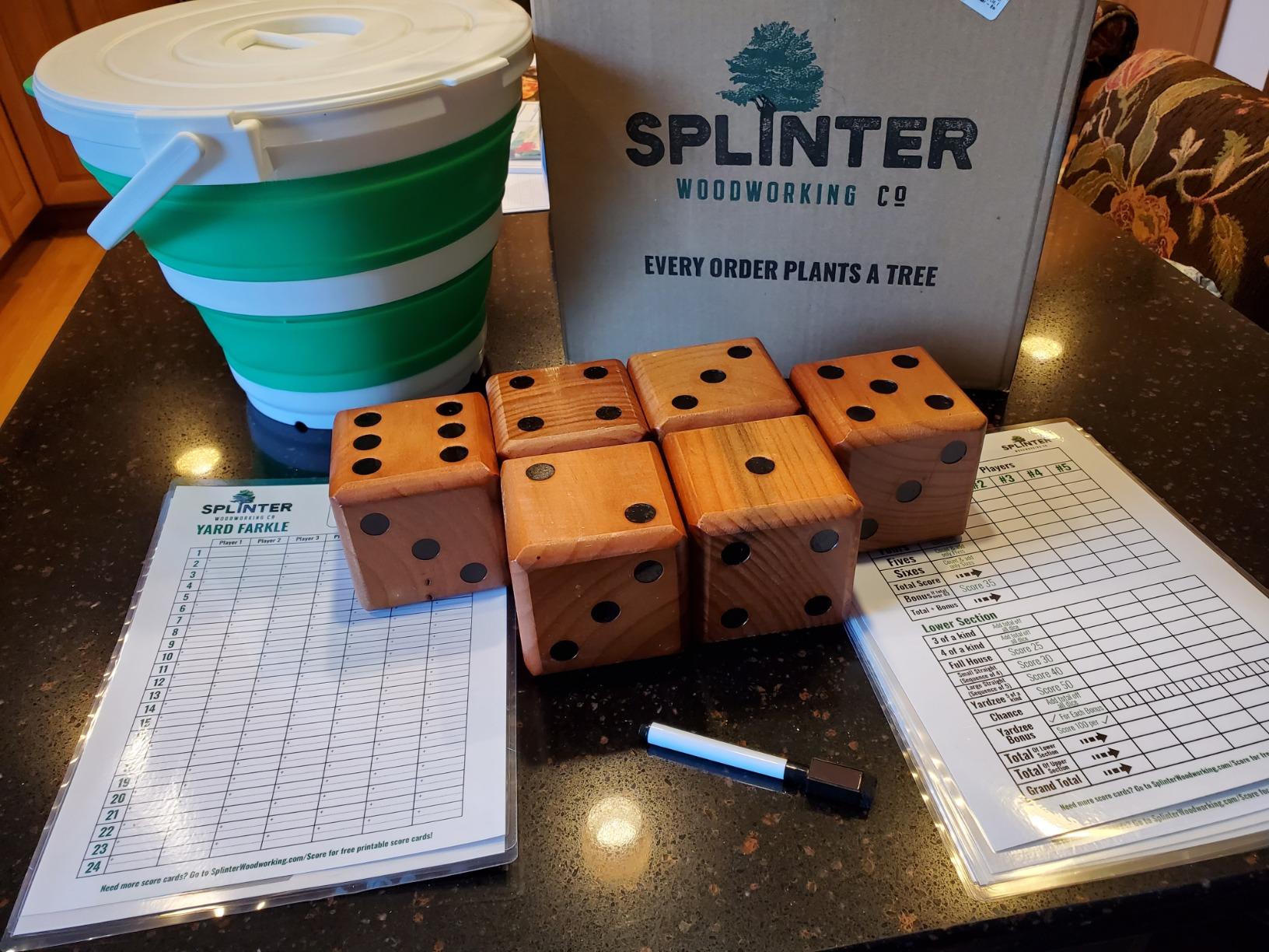 Six wooden yard dice on a kitchen counter with a collapsible bucket, laminated Yard Farkle and Yardzee score cards and a dry-erase marker