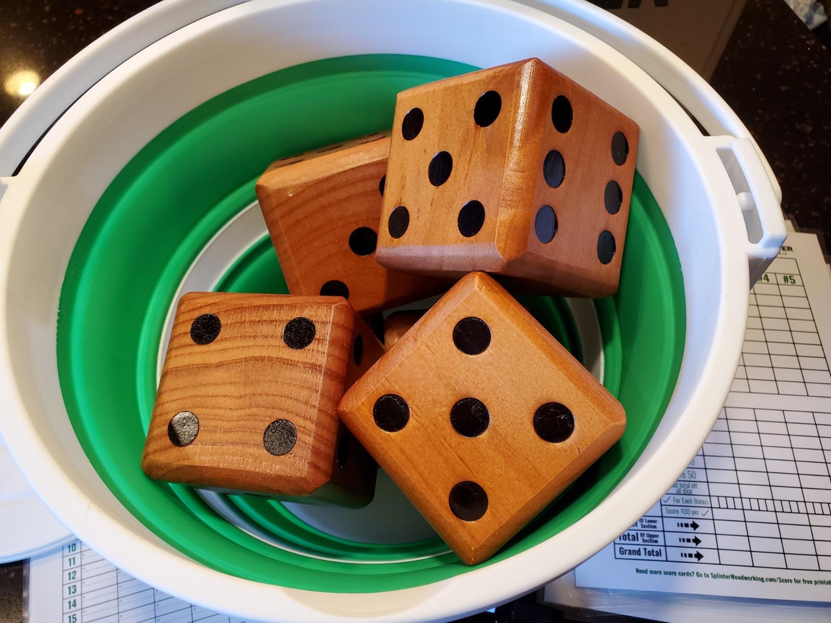 Wooden yard dice with dark pips sitting inside a collapsible green and white silicone bucket