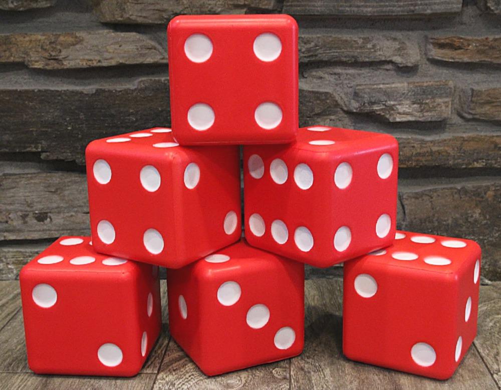 Six red foam giant dice stacked in a pyramid on a wooden deck in front of a stone wall