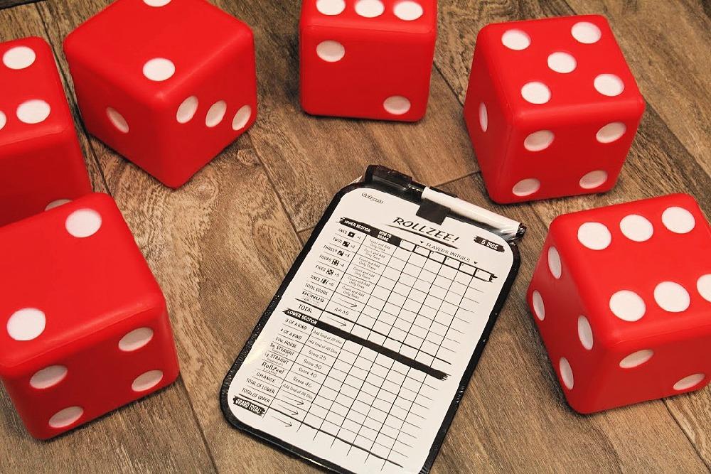 Red foam giant dice scattered around a dry-erase scoreboard on a wood floor
